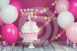 First birthday cake with a unit on a pink background with balls and paper garland.