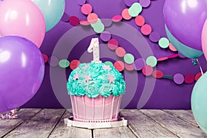 First birthday cake with a unit on a purple background with balls and paper garland.