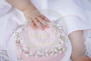 First birthday smash the cake. Cream on hands. Little caucasian baby girl celebrating first birthday with smash cake
