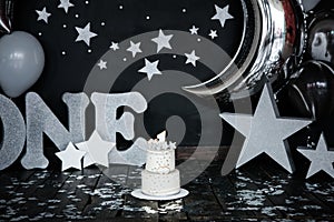 First birthday white cake with stars and candle for little baby boy and decorations for cake smash. Big silver letters ONE, silver