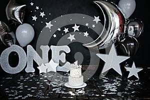 First birthday white cake with stars and candle for little baby boy and decorations for cake smash. Big silver letters ONE, silver