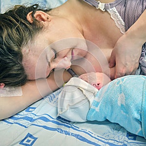 The first breast feeding of a newborn baby boy immediately after giving birth on a hospital bed in a maternity ward
