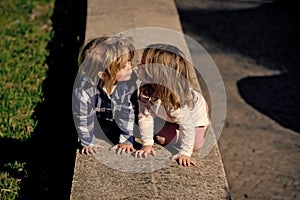 First childish love. Boy and girl kiss on stone kerb on sunny day