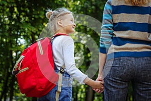 First day at school. Woman and girl with red backpack behind the back. Beginning of lessons. First day of fall. Back to