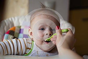 The first feeding of the baby from the spoon. Mom feeds baby homogenized chopped food with a spoon. child care.