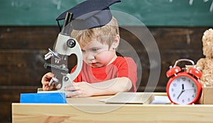 First former interested in studying, learning, education. Kid boy in academic cap work with microscope in classroom