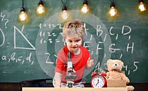 First former interested in studying, learning, education. Kid boy near microscope in classroom, chalkboard on background