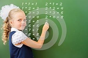 First grade schoolgirl wrote multiplication table on blackboard with chalk