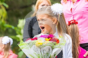 First grader with bouquet of flowers yawns at school in a crowd
