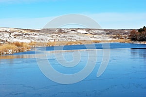 First ice on lake, withered reeds and hills with autumn yellow grass under snow and forest