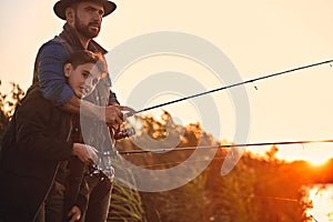 The first joint fishing of adult father and teen son in warm, sunny day.