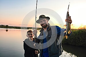 The first joint fishing of adult father and teen son in warm, sunny day.