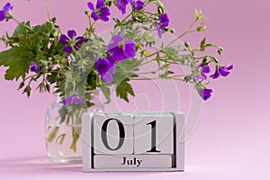 The first of July is in the yard. Desktop calendar on a delicate pink background.