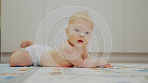 First movements of crawling on the stomach. Baby Boy lies on the mat, holding his fingers in his mouth, then begins to
