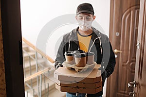 First persom view of delivery man in mask and gloves give pizza and coffe. Stay home photo