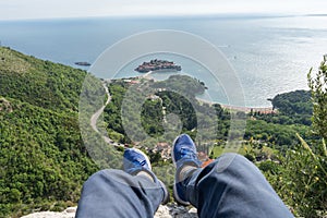 First person perspective sightseeing of sveti stefan in Budva, Montenegro. Legs with blue sneakers of a traveler in a cliff with