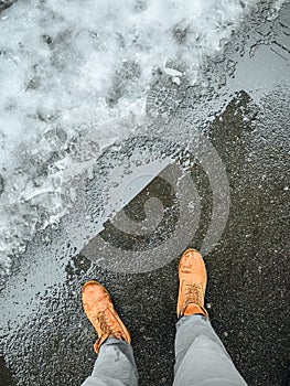 First person point of view down on the man feet wearing yellow boots. Paving tile covered with slush. Cold weather with snow