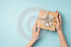 First person pov top view photo of woman`s hands holding craft paper giftbox decorated with snow branch and twine on 