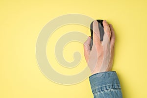 First person top view photo of female hand with black computer wireless mouse on isolated yellow background with copyspace
