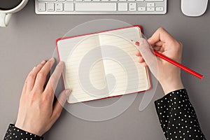 First person top view photo of female hands holding pencil over red open organizer white keyboard mouse and cup of coffee on