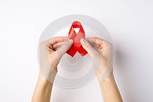 First person top view photo of girl`s hands holding red silk ribbon symbol of aids awareness on  white background with