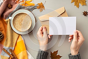 First person top view photo of girl`s hands in sweater holding envelope paper card cup of coffee saucer plaid maple leaves pine