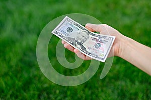 First person top view photo of hands holding fan of Dollar banknotes on park background