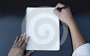 First person top view photo of male hands in black pullover writing in spiral notepad