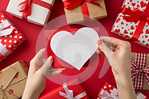 First person top view photo of saint valentine`s day decor female hands holding red envelope and paper heart over present boxes o