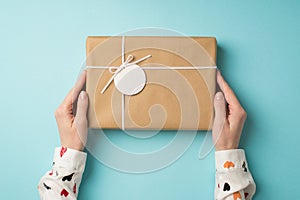 First person top view photo of valentine`s day decorations female hands in white shirt holding craft paper giftbox with small bow