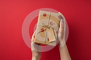 First person top view photo of valentine`s day decorations young person`s hands demonstrating craft paper giftbox with polka dot