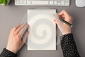 First person top view photo of woman`s hands holding pen open planner white keyboard mouse flowerpot on isolated grey background