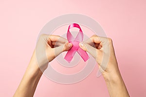 First person top view photo of woman`s hands holding pink satin ribbon with fingers symbol of breast cancer awareness on isolated