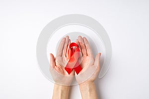 First person top view photo of woman`s hands holding red satin ribbon in palms symbol of aids awareness on isolated white