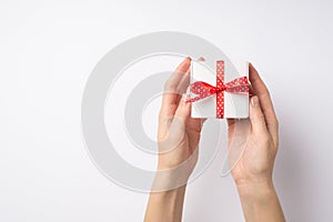 First person top view photo of woman`s hands holding small white giftbox with red dotted ribbon bow on isolated white background