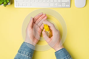 First person top view photo of woman`s hands using sanitizer spray in yellow bottle plant white keyboard mouse on isolated yellow