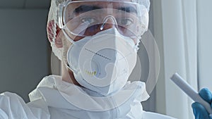 First-person view doctor scientist laboratory worker in medical protective uniform mask and glasses takes saliva sample