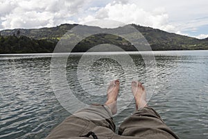 First person view of a male legs over a blue lake with watter refflections