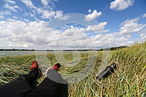 First person view on a males legs sitting on the floor by a river on a bright summers day