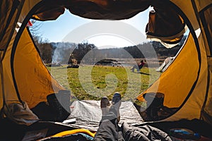 First-person view from the tent. Male feet. View of the grass, fire and river. Tourism and recreation concept. Tourist equipment.