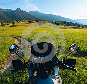 First person View tourer motorcycle steering wheel on dirt road. beautiful green field. World adventure rider. Tourist bike.