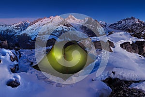 First snow in mountains. Winter camp, night, shining green tent in the snow. Night shot, long exposure, sleeping in the snow.