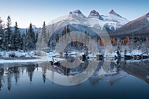 First snow Almost near perfect reflection of the Three Sisters Peaks in the Bow River. Canmore in Banff National Park Canada