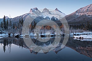 First snow Almost near perfect reflection of the Three Sisters Peaks in the Bow River. Canmore in Banff National Park Canada