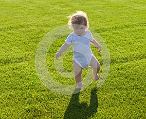 First step. Baby bare legs standing on green grass.