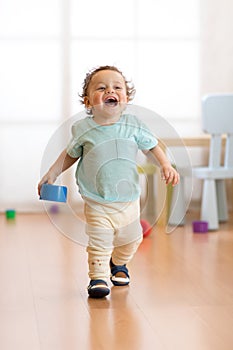 First steps of baby boy toddler learning to walk in living room. Footwear for little kids.