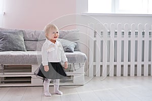 First steps of baby girl learning to walk in white sunny bedroom