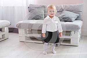 First steps of baby girl learning to walk in white sunny bedroom