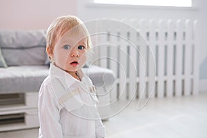 First steps of baby girl learning to walk in white sunny bedroom