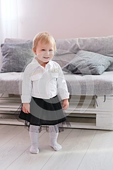 First steps of baby girl learning to walk in white sunny bedroom